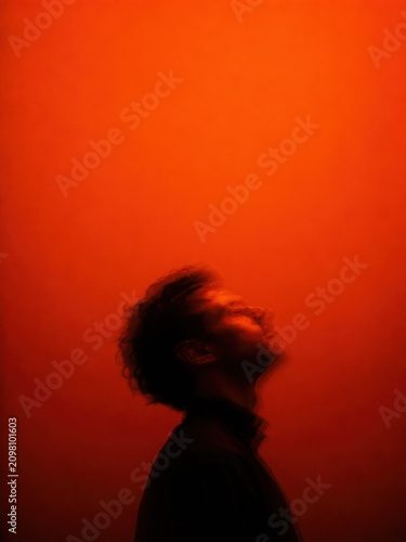 Ethereal motion blur side portrait of a man looking upwards, dreamy ghosting effect with vibrant fiery orange monochrome lighting for spiritual or psychological editorial design