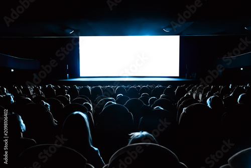 Foto Full audience seated in a dark movie theater watching a blank white cinema scree