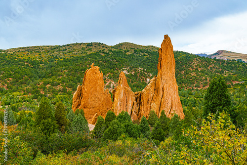Bild auf Leinwand The distinctive vertical orange spires of the Three Graces formation standing tall above a dense evergreen forest under a dramatic sky