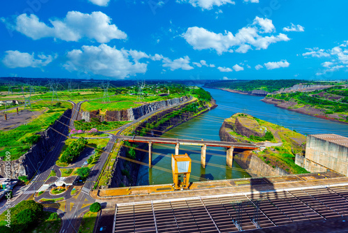Panoramic view of the Itaipu Hydroelectric Dam on the Parana River, showing the massive engineering structure, surrounding green landscape, and blue sky on the border of Brazil and Paraguay.