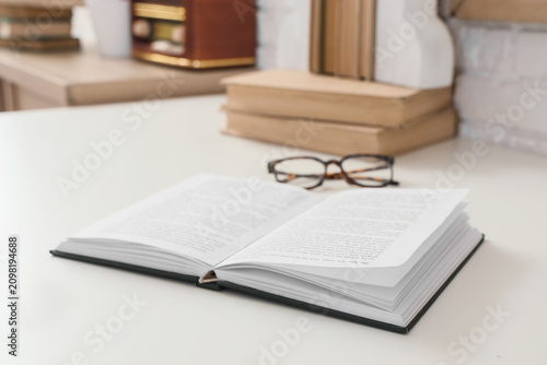 Open book with reading glasses on a white desk, education and learning concep...