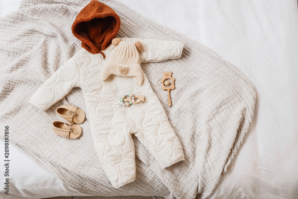Fototapeta premium Cozy baby winter outfit with quilted jumpsuit, knitted hat, moccasins, and wooden toys on a soft blanket