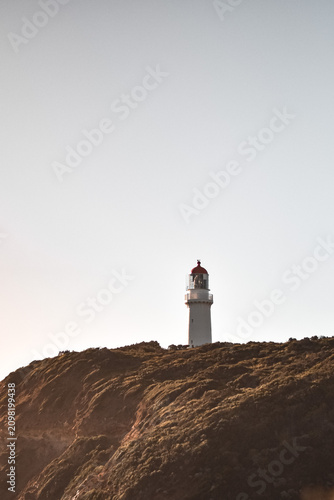 Fotografie Historic lighthouse standing on grassy hilltop against a pale sky