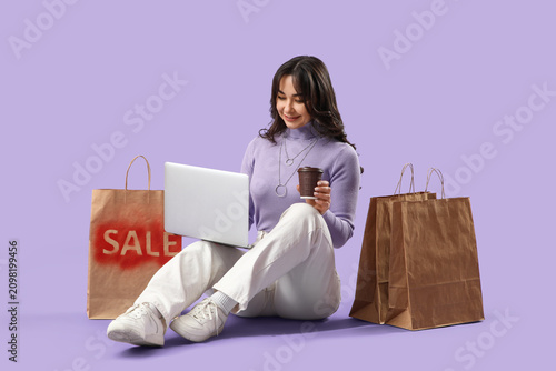 Beautiful woman with laptop and coffee shopping online on lilac background
