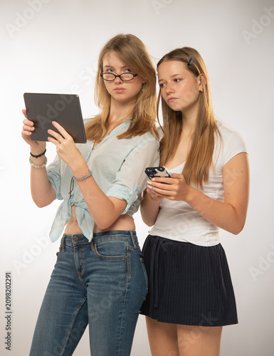 two teenage student girls using a tablet looking at the screen on a light background