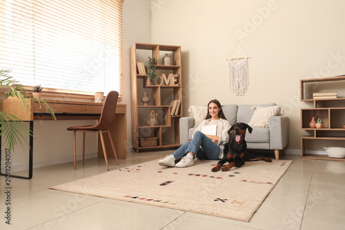 Fotografie Cute Doberman dog and beautiful young happy woman with laptop sitting on floor a