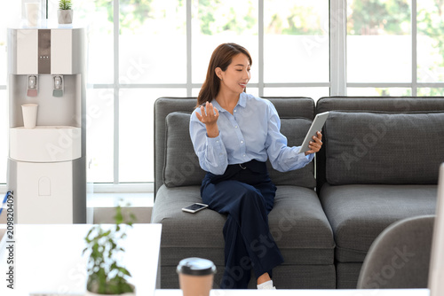 Asian businesswoman with tablet computer video chatting on sofa in office