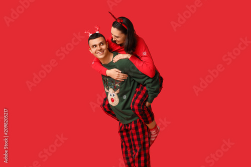 Happy young couple in Christmas pajamas having fun on red background
