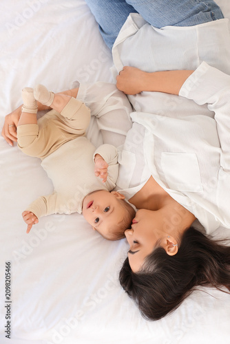 Happy mother with her little baby lying on bed, top view