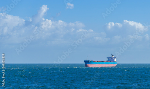 Fotografie Large industrial cargo ship lies at anchor in a brilliant blue ocean beneath a c