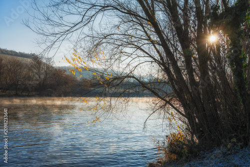 Φωτογραφία Winter river bank, fog over the river, sun through the bushes