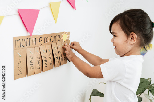 Little girl checking morning routine chart at home - Kid using DIY chore schedule - Learning and child development concept