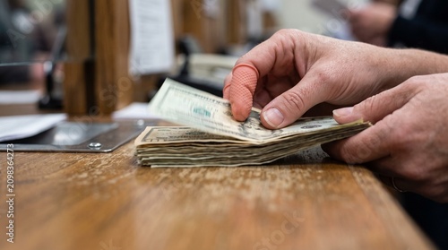 A person is counting a stack of money on a wooden table indoors.