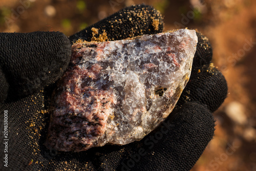 Принти на полотні Hand holding a rough piece of granite pegmatite showing crystalline texture with