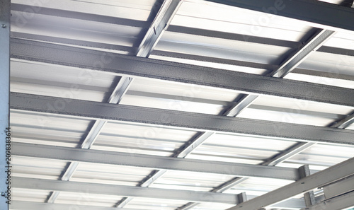 Low-angle view of a steel roof frame with metal roofing panels in a modern building. Structural steel construction, industrial architecture, and building infrastructure concept.