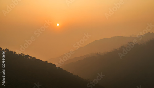 Mountain landscape covered by thick PM2.5 haze caused by forest burning, low visibility, sunrise obscured by smoke, environmental crisis in Southeast Asia, realistic landscape photography, documentary