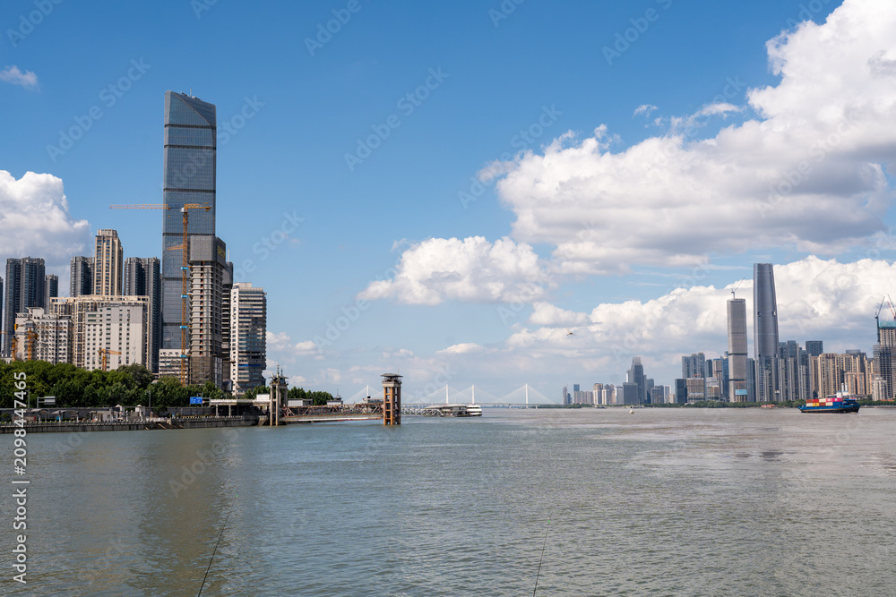 Fototapeta premium A view of the modern city skyline featuring tall buildings and skyscrapers along the river banks in Wuhan China under a bright blue sky with white clouds