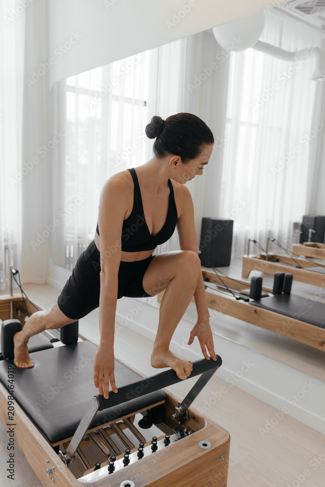 Fototapeta premium Slim woman exercising on Pilates reformer machine during fitness training