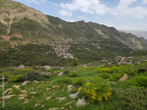Lush spring landscape with a mountain village, rocky slopes, green meadows, wildflowers, and dramatic peaks beneath a partly cloudy sky.
📍 Kamalla village, Hawraman Takht, Kurdistan 