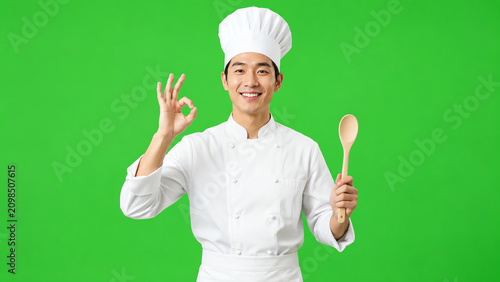 A cheerful chef dressed in uniform holds a wooden spoon and signals perfection with a gesture against a green background.
