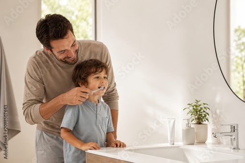 Parent Helping Young Child Brush Teeth in Warm Modern Bathroom