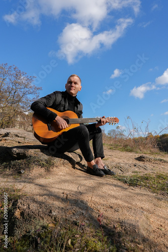 Portrait of smiling caucasian artist plays wooden acoustic guitar in autumnal park. Young songwriter plays string musical instrument hobby outside in nature fall time. Audio music healing in natural