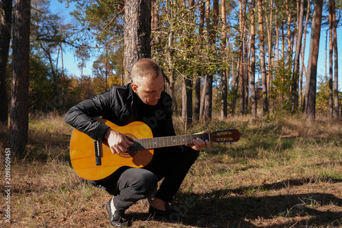 Portrait of smiling caucasian artist plays wooden acoustic guitar in autumnal park. Young songwriter plays string musical instrument hobby outside in nature fall time. Audio music healing in natural