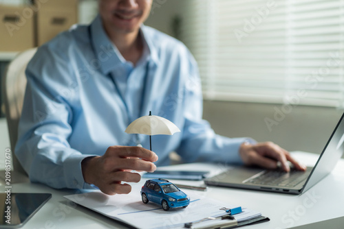 Close-up of insurance agent hand holding small umbrella over toy car for auto insurance and vehicle protection concept.