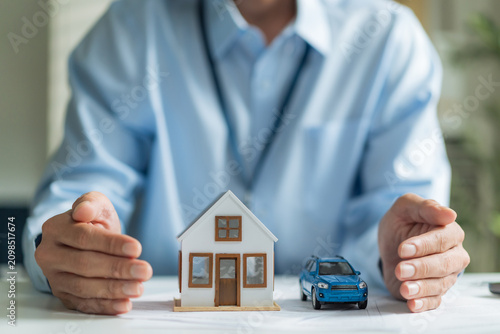 Cuadro en lienzo Close-up of businessman hands protecting house model and toy car for real estate and auto insurance concept