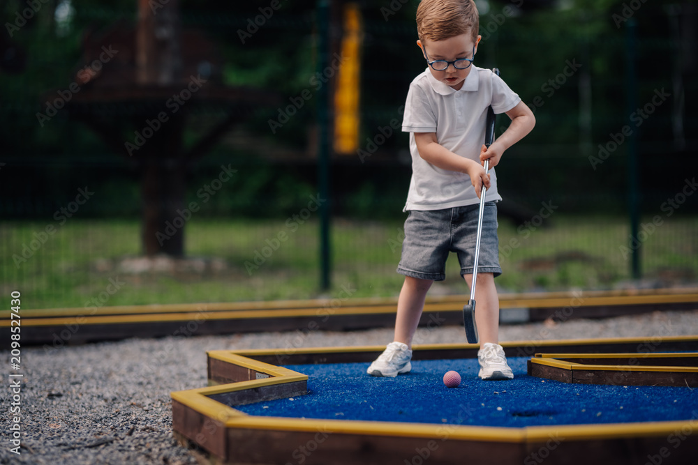 Obraz premium Boy playing mini golf with concentration outdoors