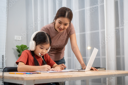 Canvastavla Mother helping her daughter study and write homework at home beside a laptop