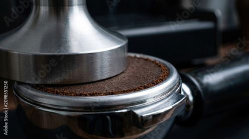 Espresso preparation, metal tamper pressing ground coffee in portafilter, barista making professional caffeine drink, morning routine concept.