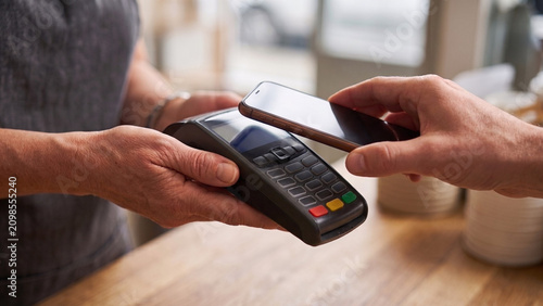 Customer making a contactless smartphone payment using a card terminal at checkout. Fast digital transactions simplify everyday purchases for businesses and consumers.