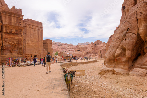 Tourists pass Bedouin markets, rock tombs and caves on the sandy Siq path through the Street of Facades in the ancient city of Petra, Jordan.