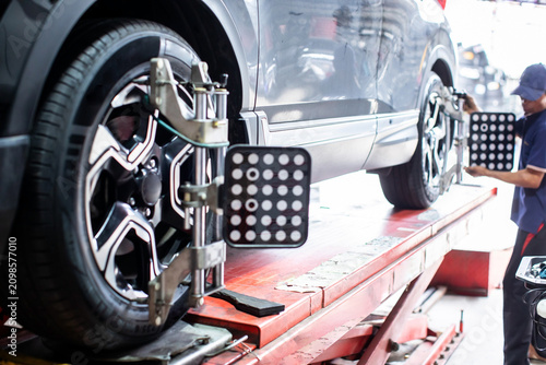 Selective focus to car body with blurry modern 3D wheel alignment equipment clamp on SUV tire with technician working on digital tracking system at automotive repair shop.