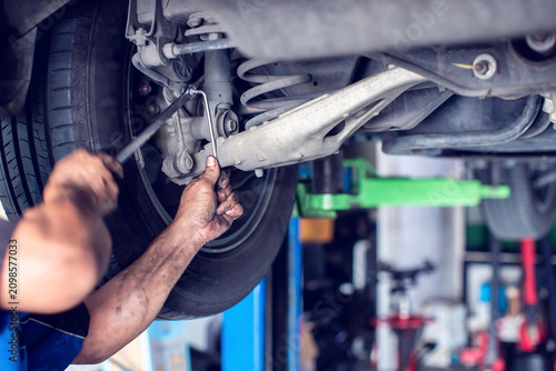 Fotografie Selective focus to hands of professional mechanic using a wrench tool to repair and adjust car rear suspension system in auto service shop