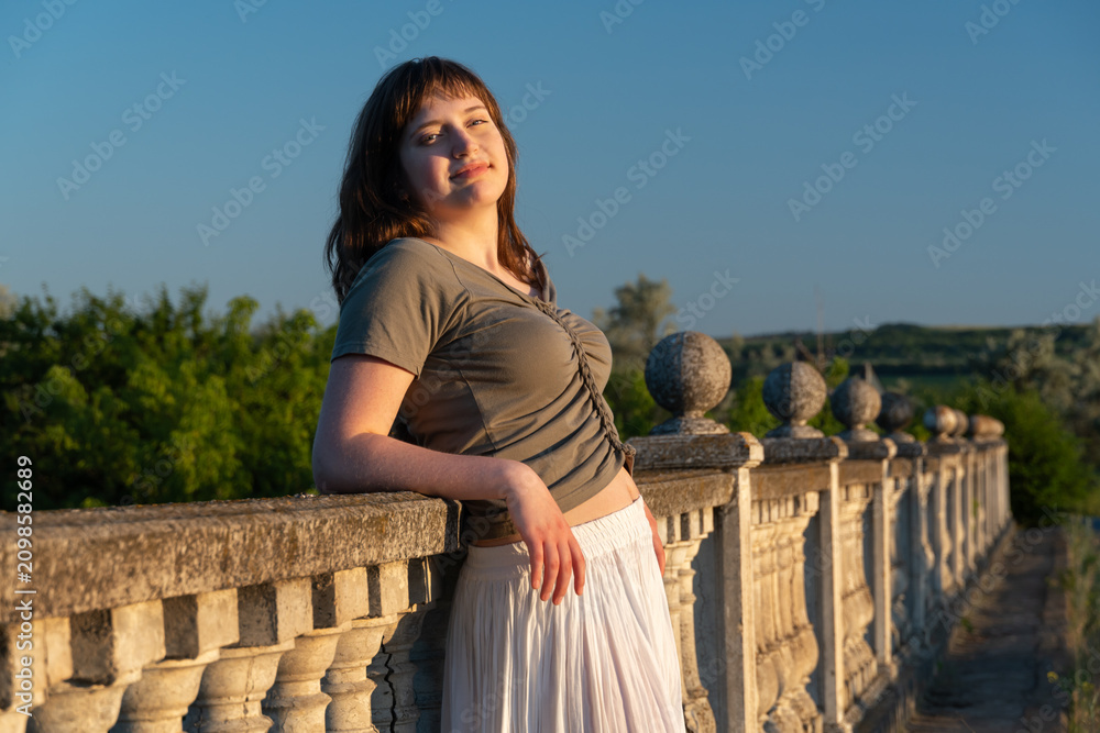 Obraz premium Young woman leaning on stone balustrade during golden hour