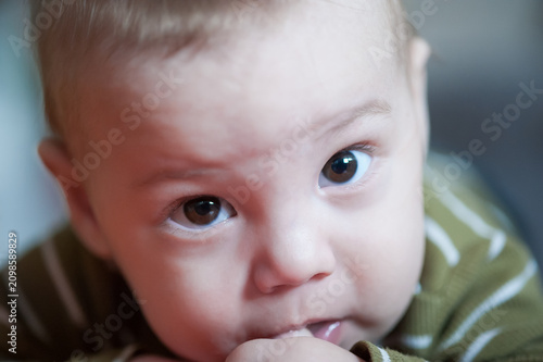 An extreme closeup of a sweet baby's face, displaying wide brown eyes full of curiosity. The infant gently sucks on a finger, absorbed in exploring sensations within a peaceful home setting