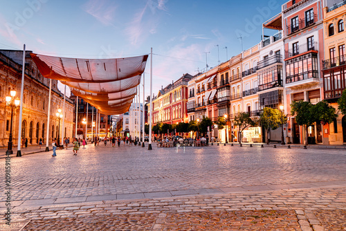 People in illuminated town square in Seville, city lights, tourists, nightlife on streets of Spanish city, Andalusia.