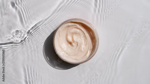 A jar of white cream on a water surface. Splash of water, sunlight and shadows. Layout for advertising goods, cosmetic products. Medical skin care, body care. High quality 4k footage