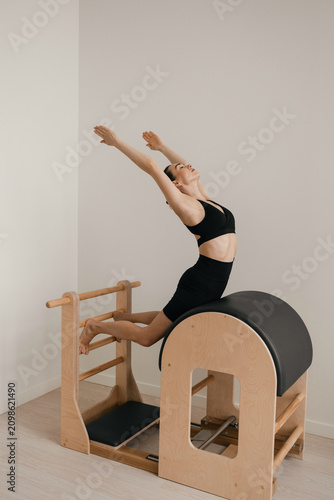 Woman performing Pilates exercises on modern Pilates ladder barrel equipment, showing specialized apparatus, controlled posture and contemporary Pilates practice in a professional studio environment.