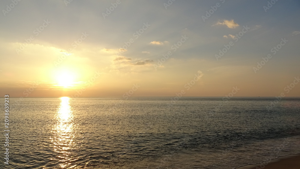 Obraz premium Serene Sunrise Beach with Soft Sunlight. A peaceful and tranquil dawn scene at a sandy beach in Gangneung, showing the soft morning sun rising above the quiet ocean with gentle waves washing ashore.