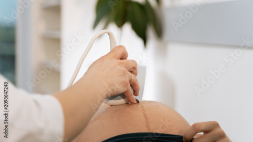 Sonographer gliding ultrasound probe over pregnant belly during routine prenatal appointment