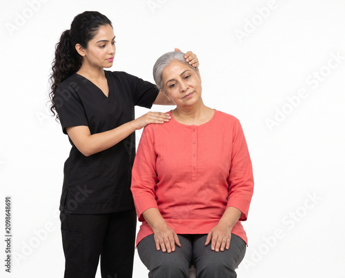 Young Indian physiotherapist assisting senior Indian woman with seated shoulder mobility rehabilitation exercise isolated on white background for physiotherapy orthopedic care and senior wellness