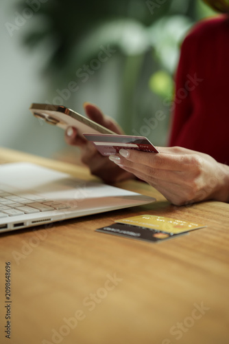 Woman holding a credit card and smartphone while shopping online with a laptop, representing secure digital payment and e-commerce.