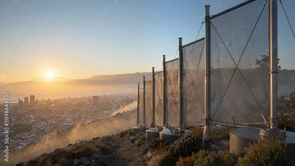 Fototapeta premium Sunset over city with fog and barriers on hilltop, showing skyline and landscape beyond