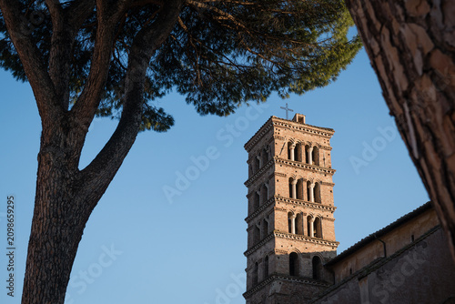 The medieval Romanesque bell tower of the Basilica of Sant'Alessio framed by pine trees in the Garden of Sant'Alessio on Aventine Hill in Rome, Italy