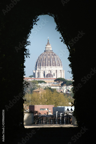 The dome of St. Peter's Basilica framed by a garden hedge tunnel through the Aventine Keyhole in Rome, Italy