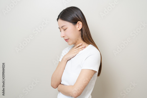 Foto Sickness in inflaming asian young woman, girl use hand check self touch at sore throat, pain thyroid gland on neck or disease reflux, acid of suffer people on wall background