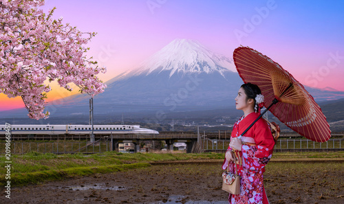 Принти на полотні Asian woman wearing traditional red kimono with paper umbrella, cherry blossoms, shinkansen bullet train, and Mount Fuji during sunset in Japan